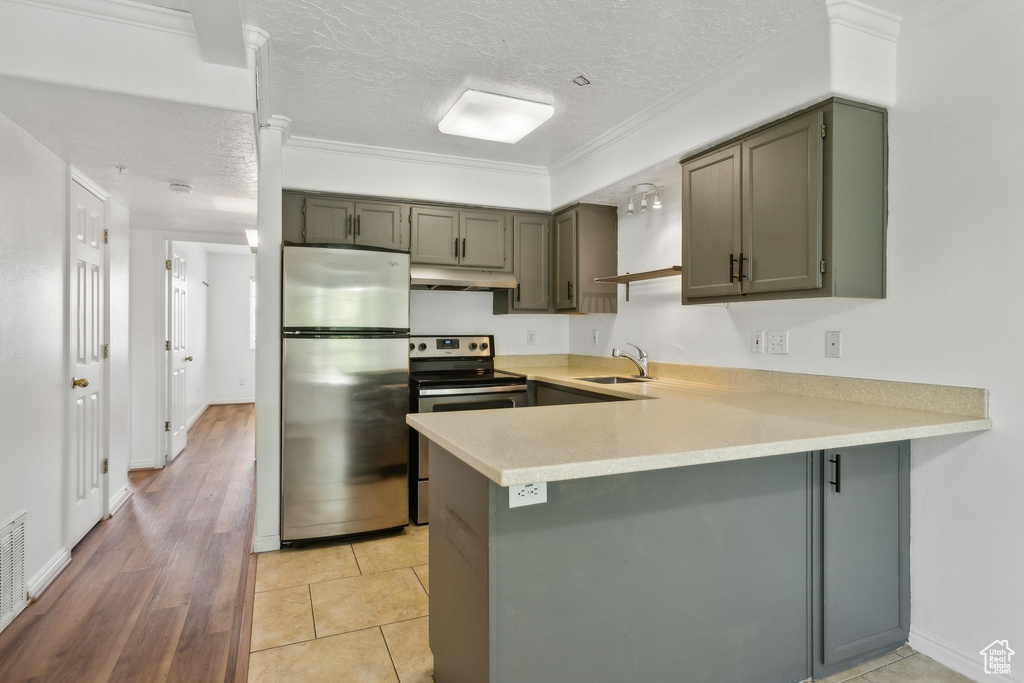 Kitchen featuring stainless steel appliances, under cabinet range hood, a peninsula, light countertops, and a textured ceiling