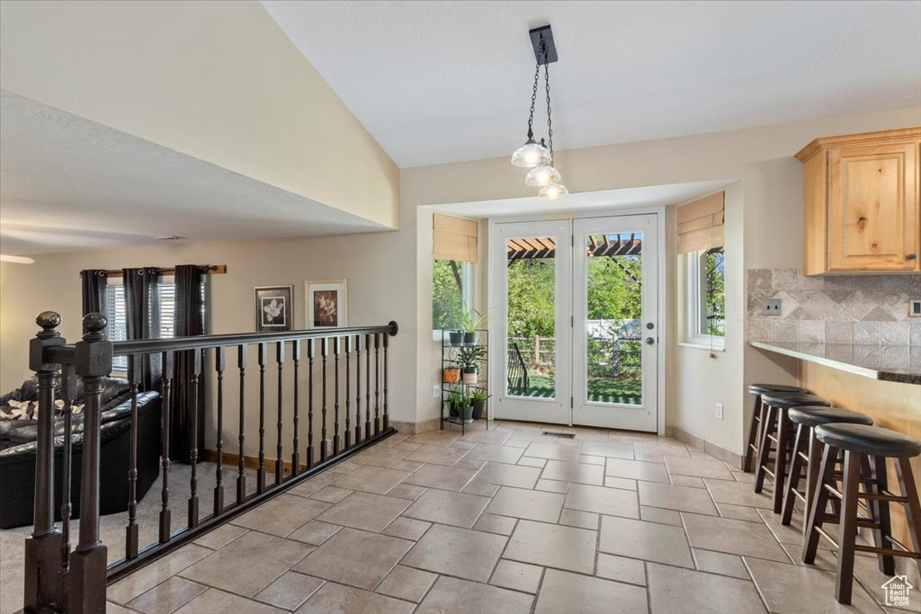 Doorway featuring baseboards, light stone finish flooring, and vaulted ceiling