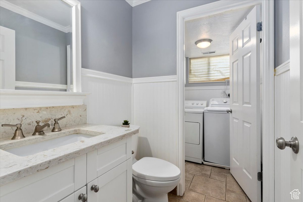 Bathroom featuring washing machine and dryer, toilet, wainscoting, ornamental molding, and vanity