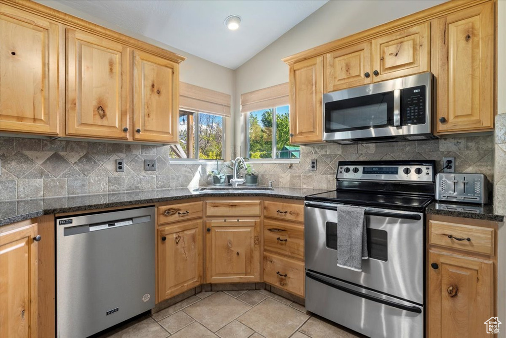 Kitchen featuring stainless steel appliances, a sink, vaulted ceiling, tasteful backsplash, and light tile patterned flooring