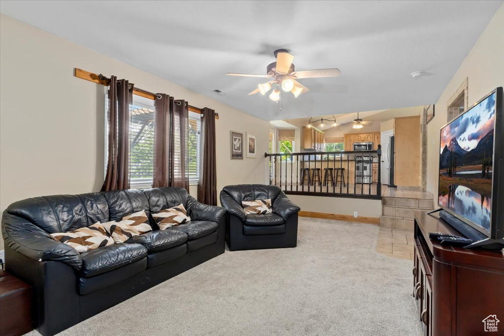 Living area featuring light colored carpet, a ceiling fan, and baseboards