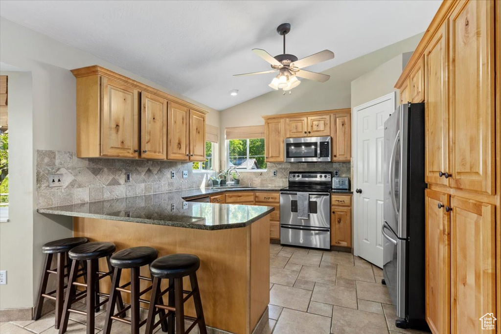 Kitchen with appliances with stainless steel finishes, a peninsula, a sink, lofted ceiling, and decorative backsplash