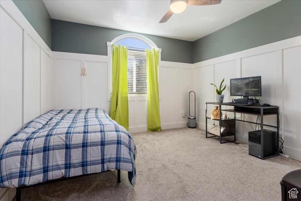 Bedroom with a decorative wall, carpet floors, wainscoting, and a ceiling fan