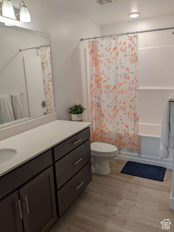Full bath with shower / tub combo with curtain, vanity, toilet, wood finished floors, and visible vents