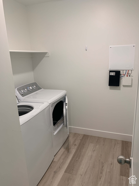 Washroom with laundry area, baseboards, washing machine and dryer, and light wood-type flooring