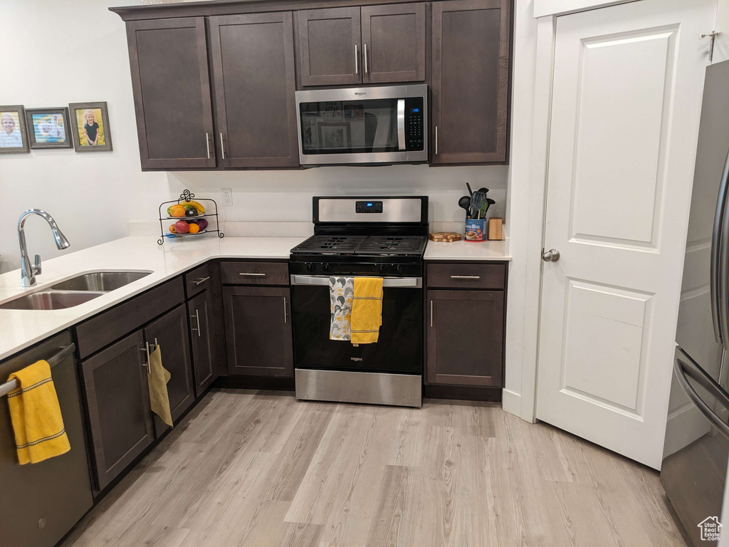 Kitchen with dark brown cabinets, appliances with stainless steel finishes, a sink, and light wood-style floors