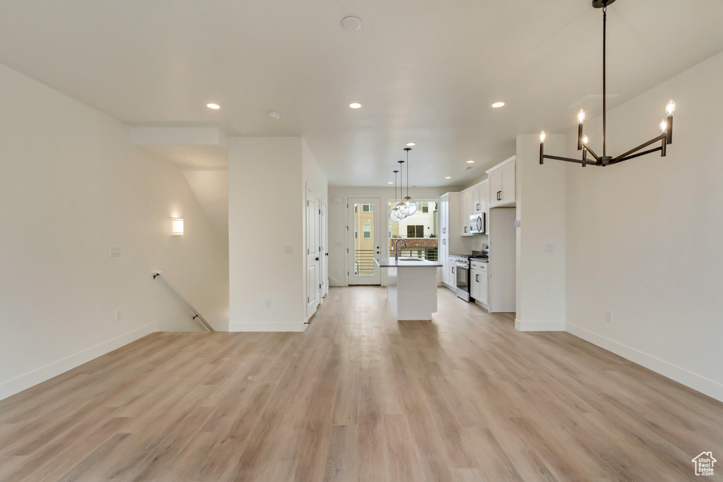 Unfurnished living room with recessed lighting, a chandelier, baseboards, and light wood-style floors