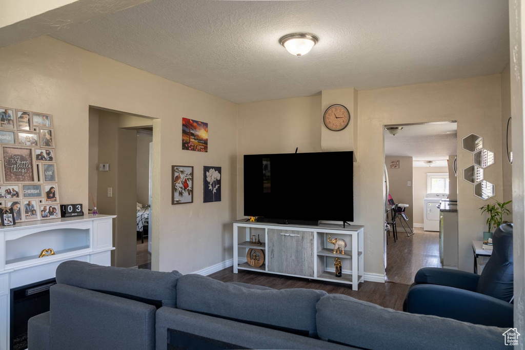 Living room featuring washer / dryer, a textured ceiling, wood finished floors, and baseboards