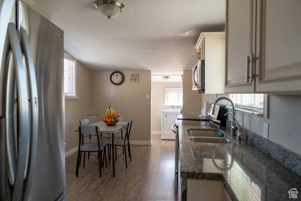 Kitchen with a sink, washer / clothes dryer, dark stone countertops, a textured ceiling, and appliances with stainless steel finishes