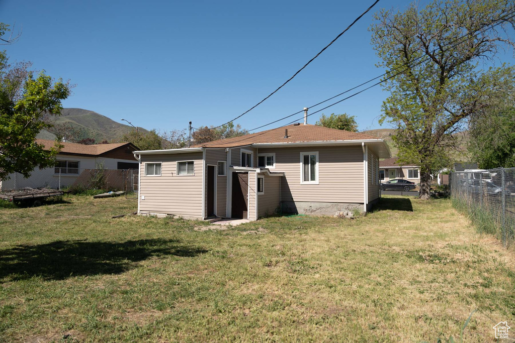 Rear view of property with a mountain view, fence, and a lawn