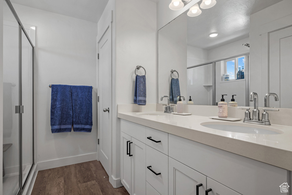 Full bathroom with a shower stall, wood finished floors, double vanity, and baseboards