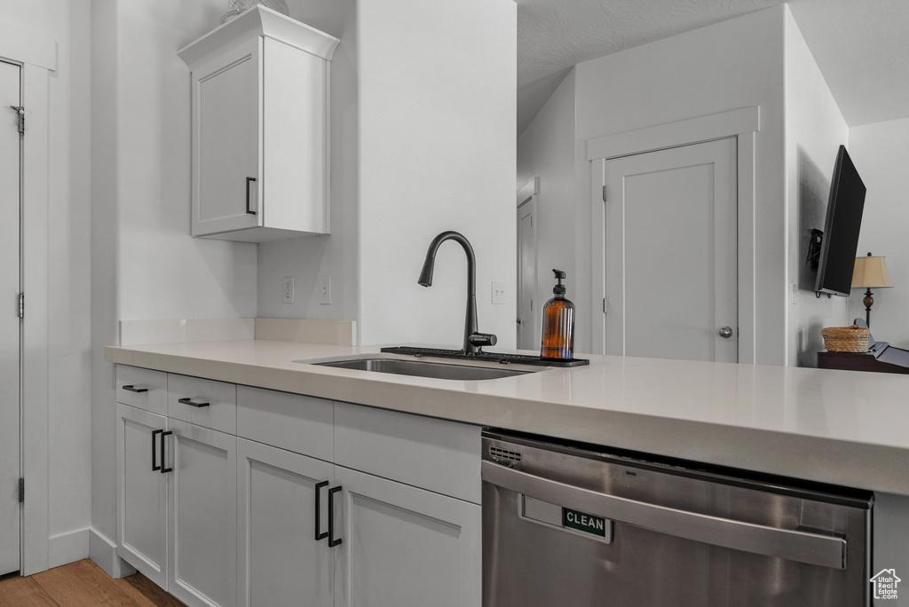 Kitchen with stainless steel dishwasher, a sink, light wood-style floors, white cabinetry, and light countertops