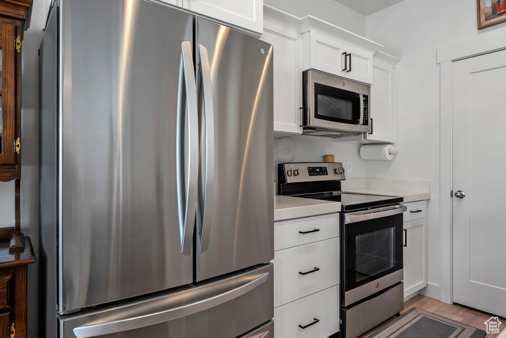 Kitchen featuring appliances with stainless steel finishes, light countertops, white cabinets, and light wood-style floors
