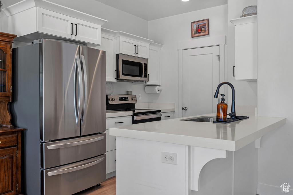 Kitchen featuring appliances with stainless steel finishes, a sink, white cabinets, a peninsula, and light countertops