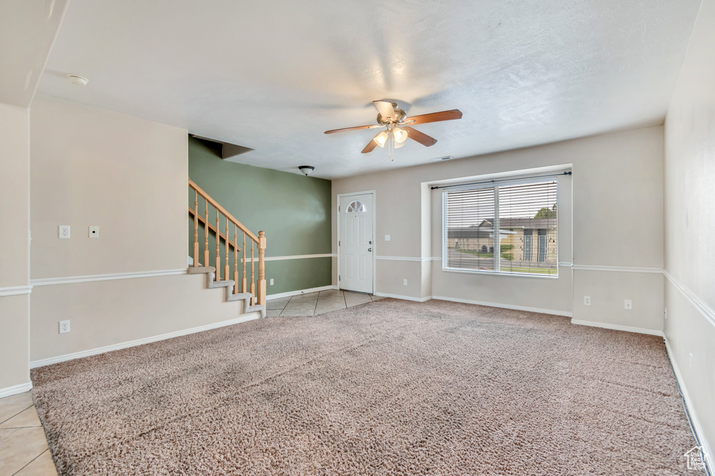 Foyer entrance with ceiling fan, stairway, baseboards, and light colored carpet