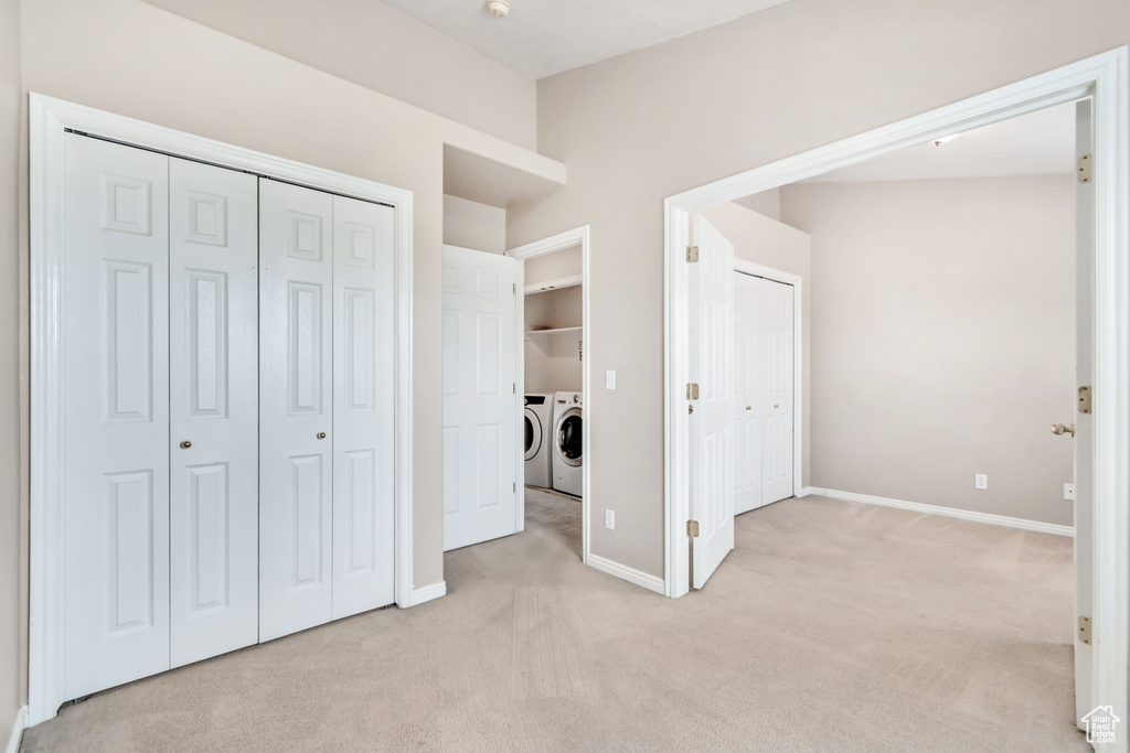 Unfurnished bedroom featuring independent washer and dryer, light colored carpet, baseboards, and a closet