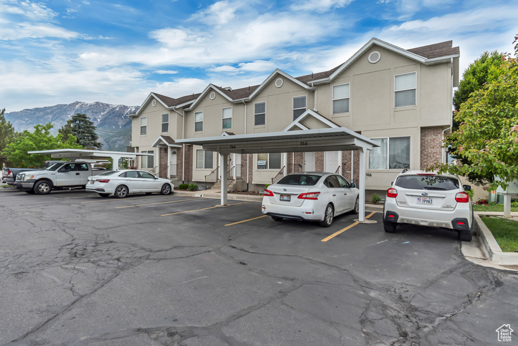 Townhome / multi-family property with covered and uncovered parking, a mountain view, and stucco siding