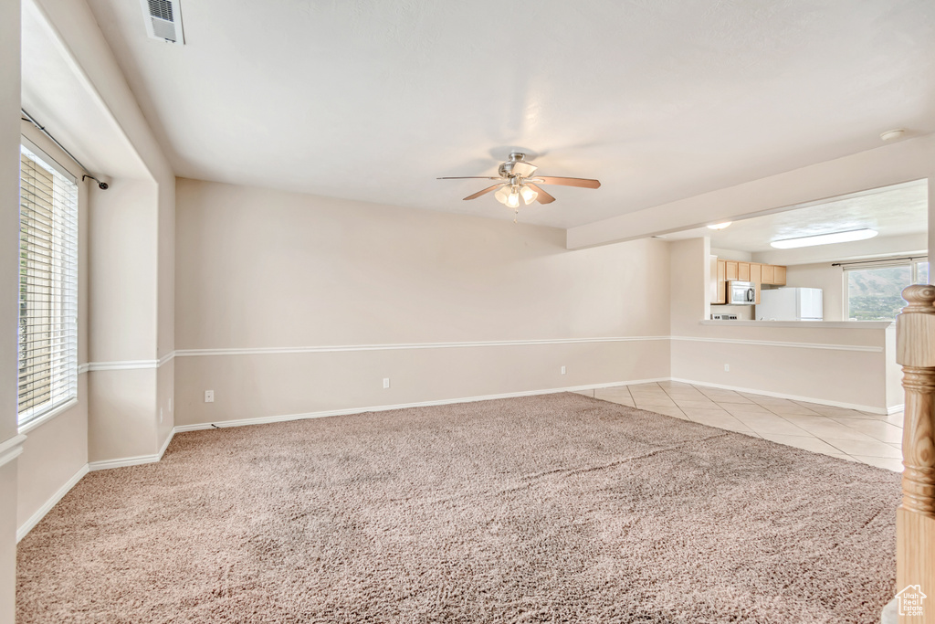Empty room featuring ceiling fan, light colored carpet, baseboards, and plenty of natural light