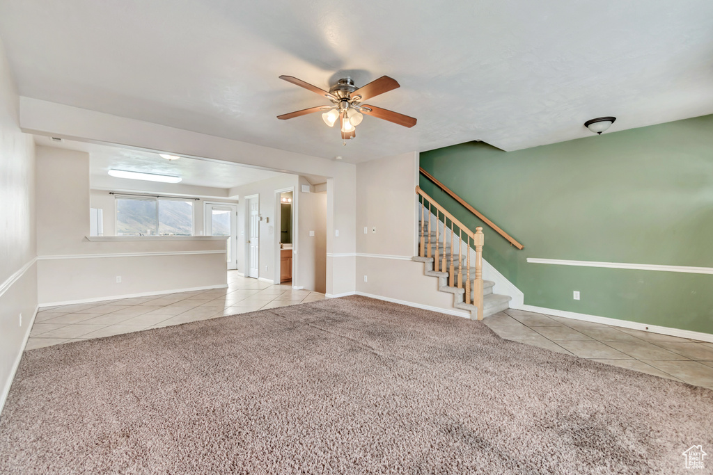 Unfurnished living room featuring tile patterned flooring, a ceiling fan, stairway, carpet floors, and baseboards