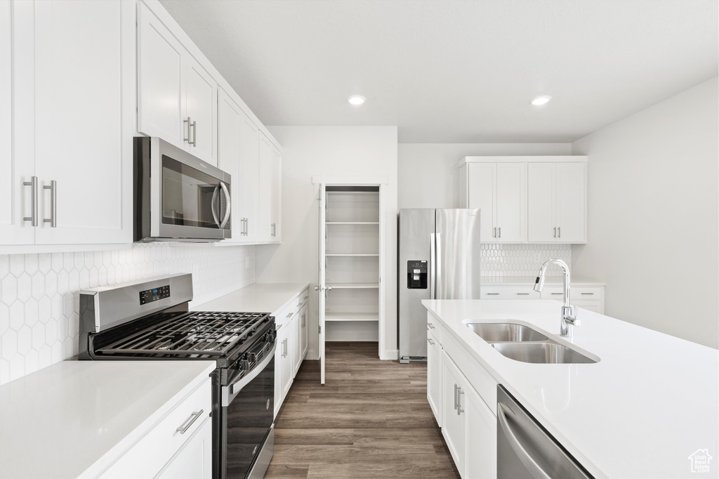Kitchen featuring appliances with stainless steel finishes, light countertops, backsplash, wood finished floors, and white cabinetry