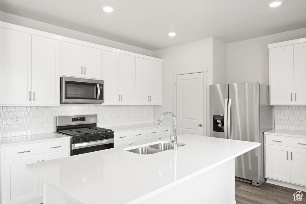 Kitchen with stainless steel appliances, a center island with sink, light countertops, white cabinetry, and recessed lighting