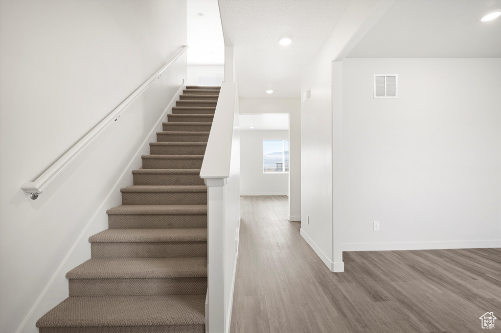 Stairs with wood finished floors and recessed lighting