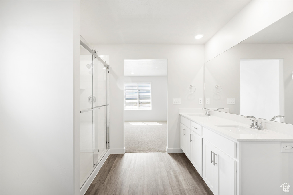 Full bath with double vanity, wood finished floors, a shower with shower door, and recessed lighting