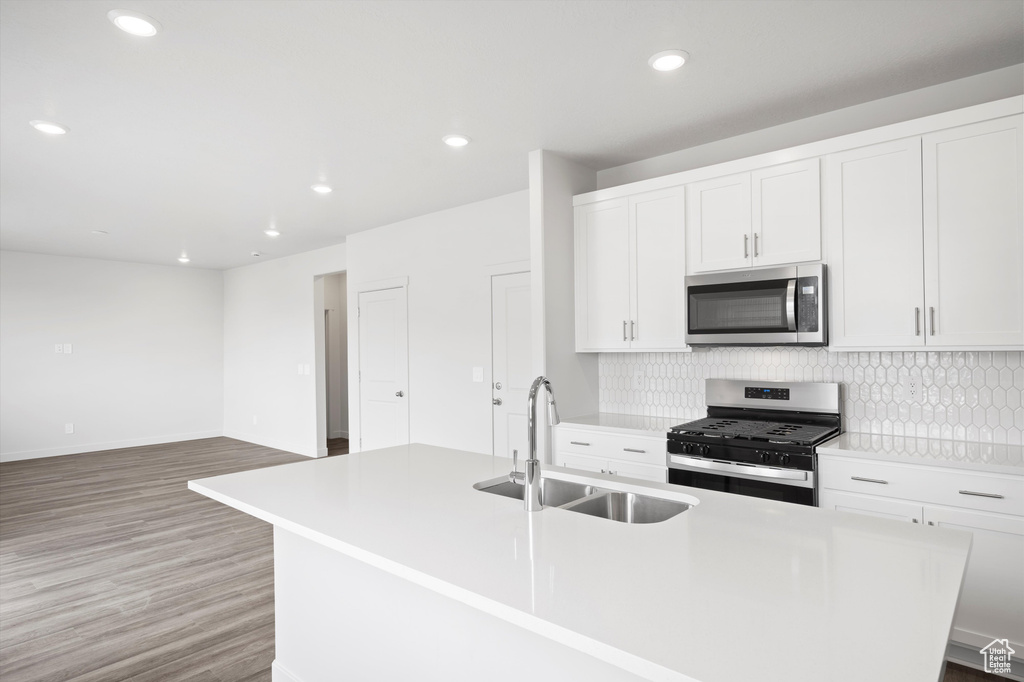 Kitchen featuring appliances with stainless steel finishes, an island with sink, backsplash, light wood-style floors, and white cabinetry