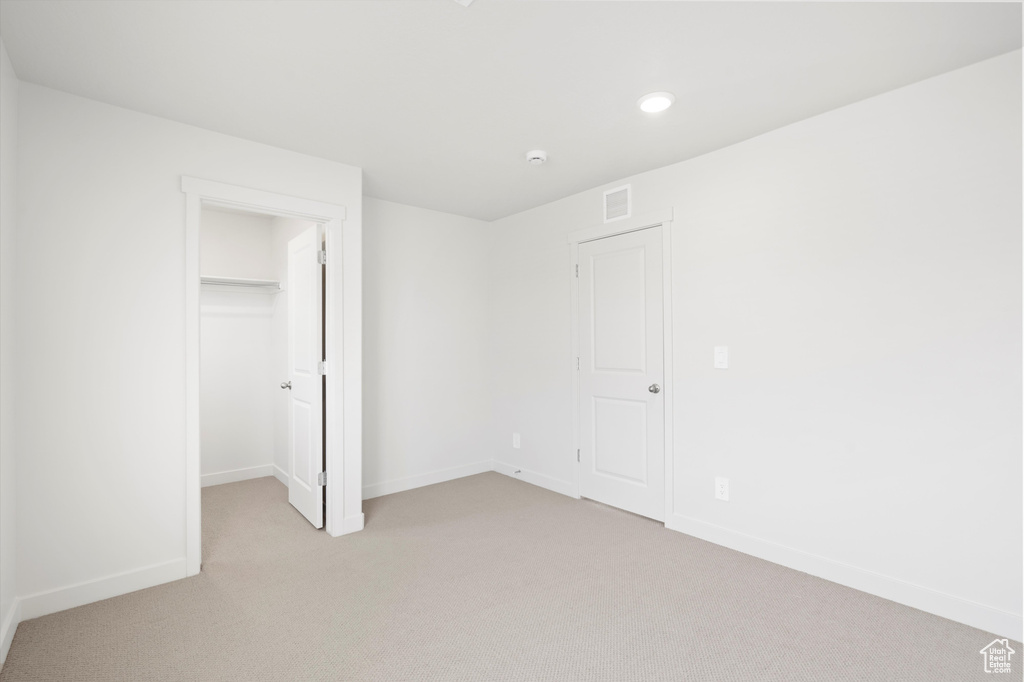 Unfurnished bedroom with light carpet, a walk in closet, and recessed lighting