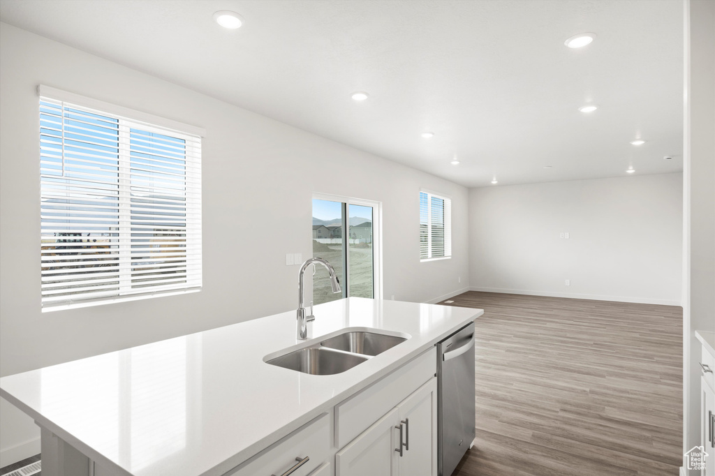 Kitchen with light wood-type flooring, dishwasher, recessed lighting, light countertops, and an island with sink