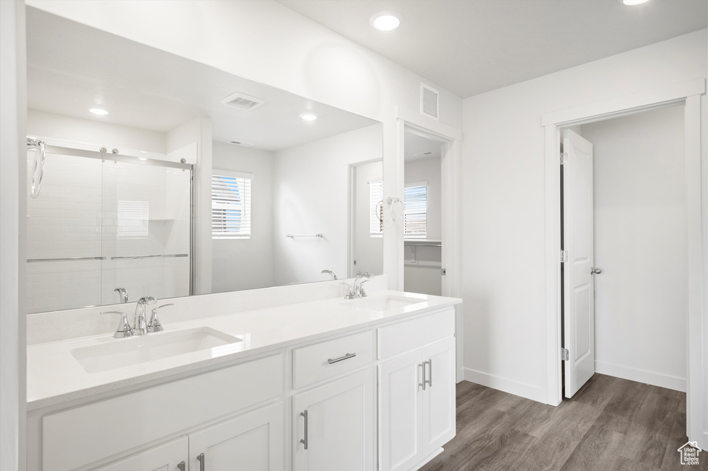 Bathroom featuring wood finished floors, a shower stall, double vanity, and recessed lighting