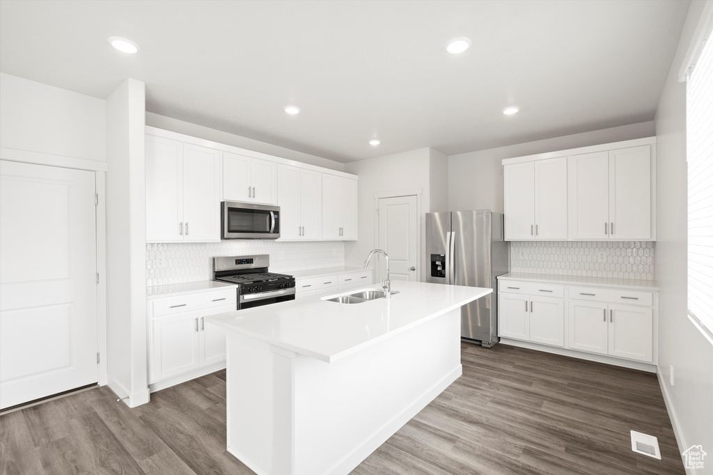 Kitchen featuring appliances with stainless steel finishes, decorative backsplash, a kitchen island with sink, dark wood-type flooring, and recessed lighting