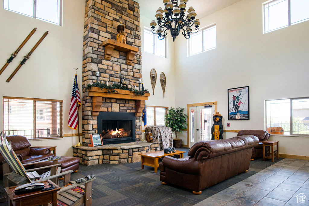 Living area with a healthy amount of sunlight, a high ceiling, a stone fireplace, and a notable chandelier