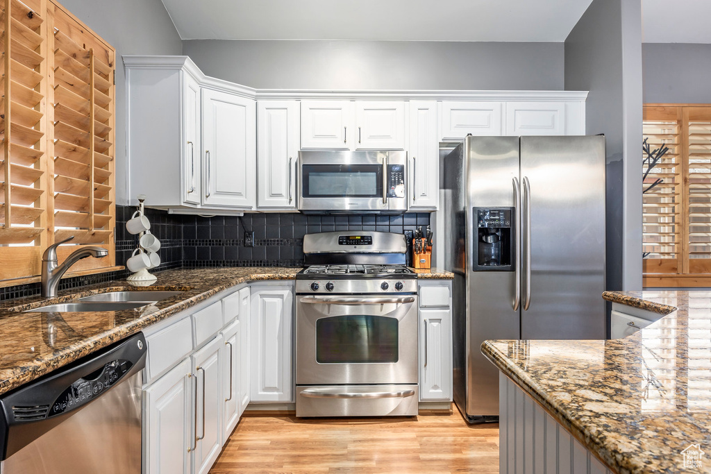 Kitchen featuring light wood-type flooring, dark stone counters, white cabinets, a sink, and stainless steel appliances