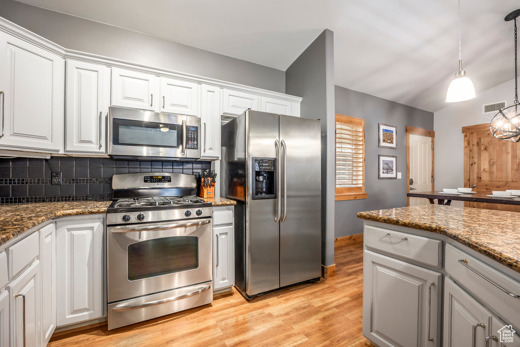Kitchen with light wood finished floors, stainless steel appliances, white cabinetry, backsplash, and visible vents