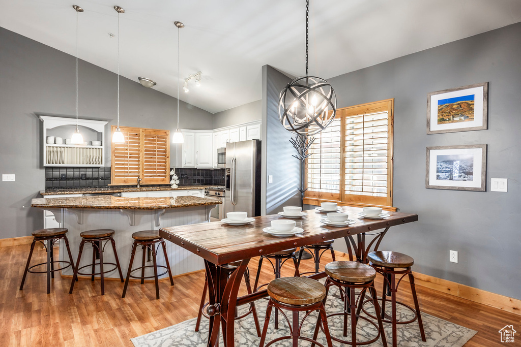 Dining space with baseboards, high vaulted ceiling, and light wood-type flooring