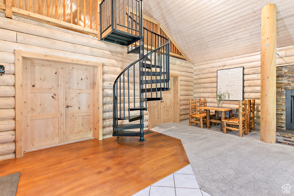 Interior space with stairway, a high ceiling, a stone fireplace, and log walls