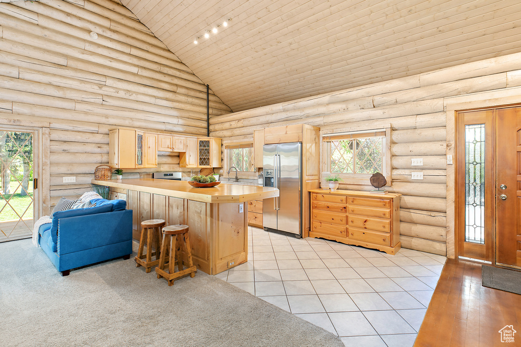 Kitchen featuring a peninsula, stainless steel appliances, high vaulted ceiling, log walls, and light brown cabinets