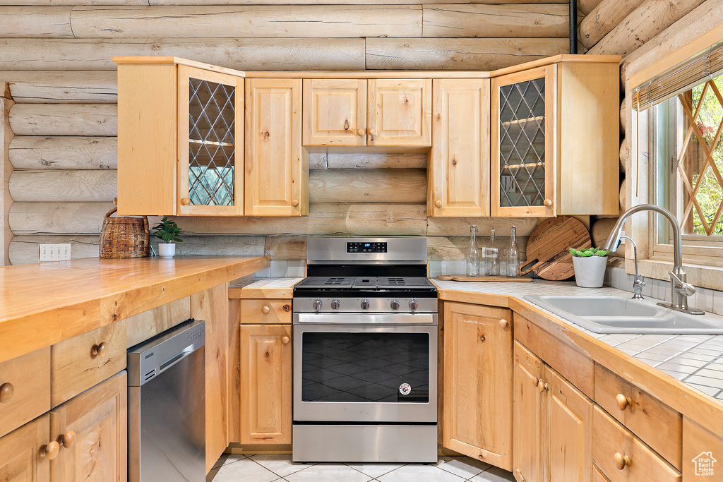Kitchen featuring light brown cabinets, rustic walls, appliances with stainless steel finishes, and a sink
