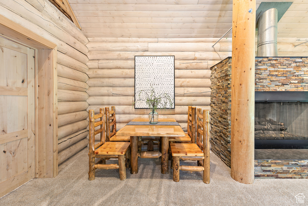 Carpeted dining room featuring wood ceiling, rustic walls, and a stone fireplace