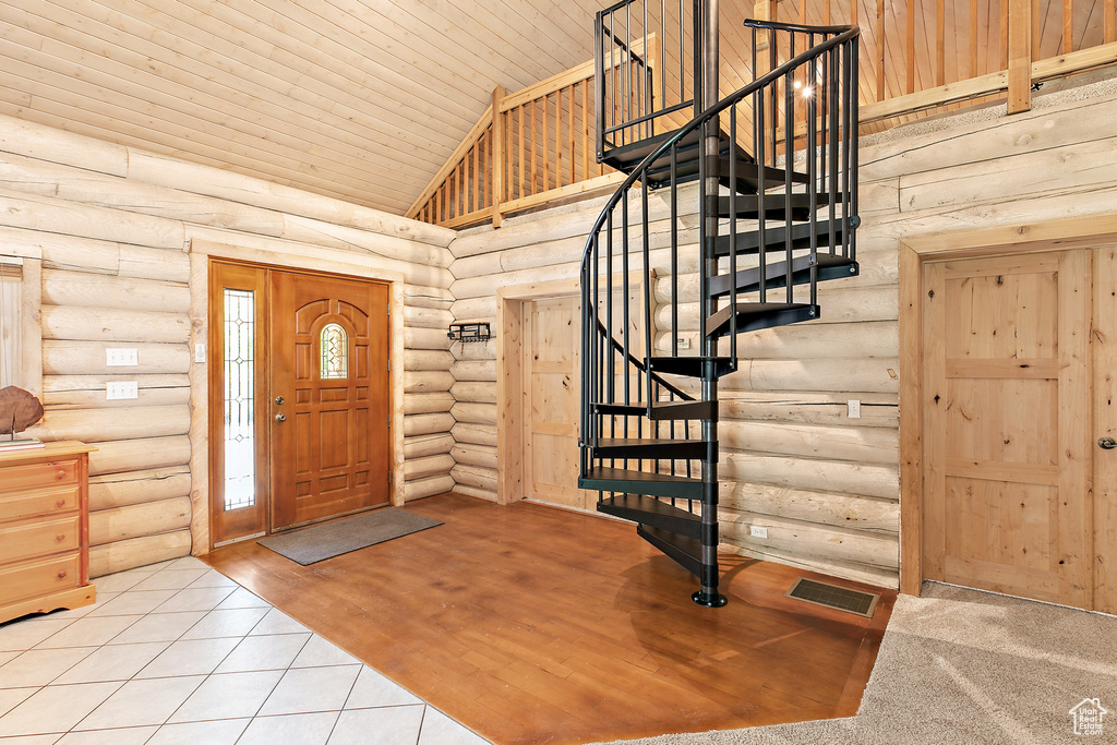 Tiled foyer featuring stairs, rustic walls, high vaulted ceiling, and visible vents