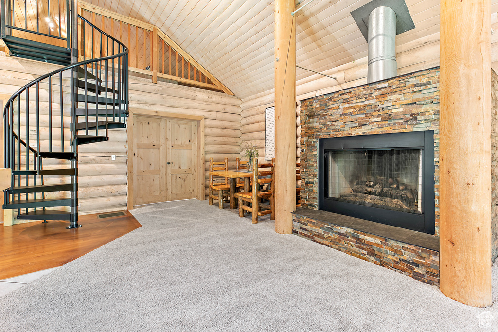 Interior space featuring a fireplace with raised hearth, log walls, visible vents, wood ceiling, and stairway