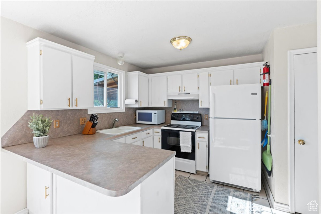 Kitchen with white appliances, a peninsula, a sink, under cabinet range hood, and backsplash