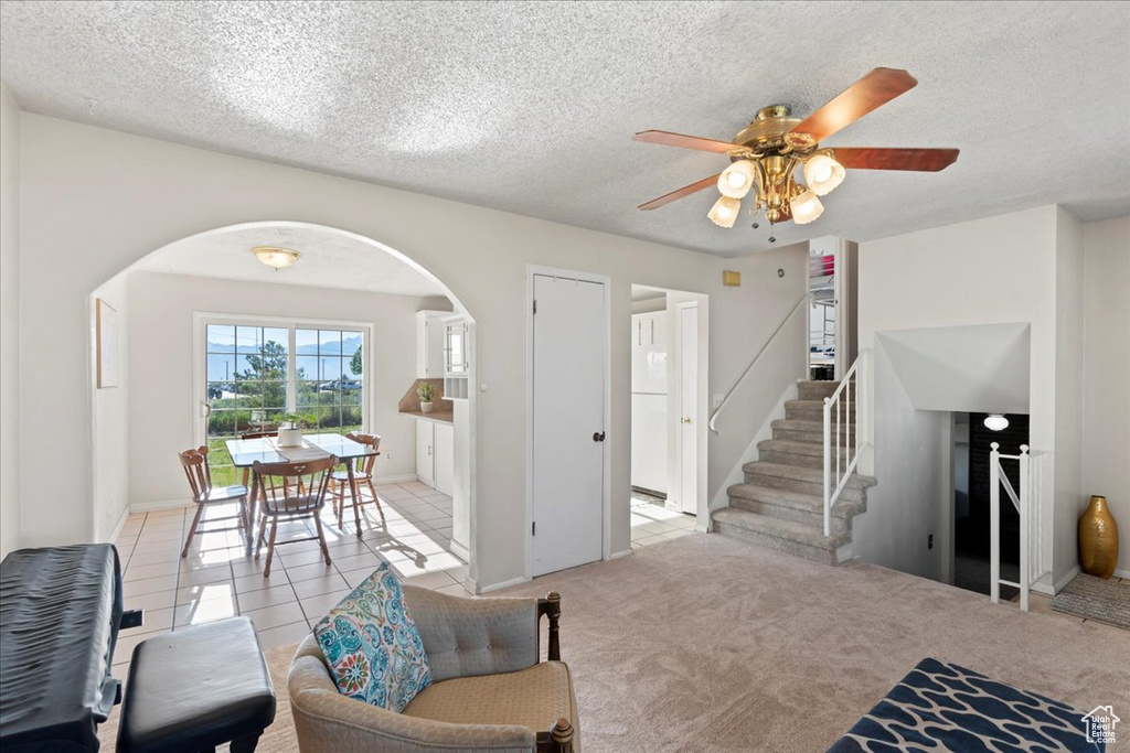 Living area with arched walkways, ceiling fan, stairway, a textured ceiling, and light tile patterned flooring