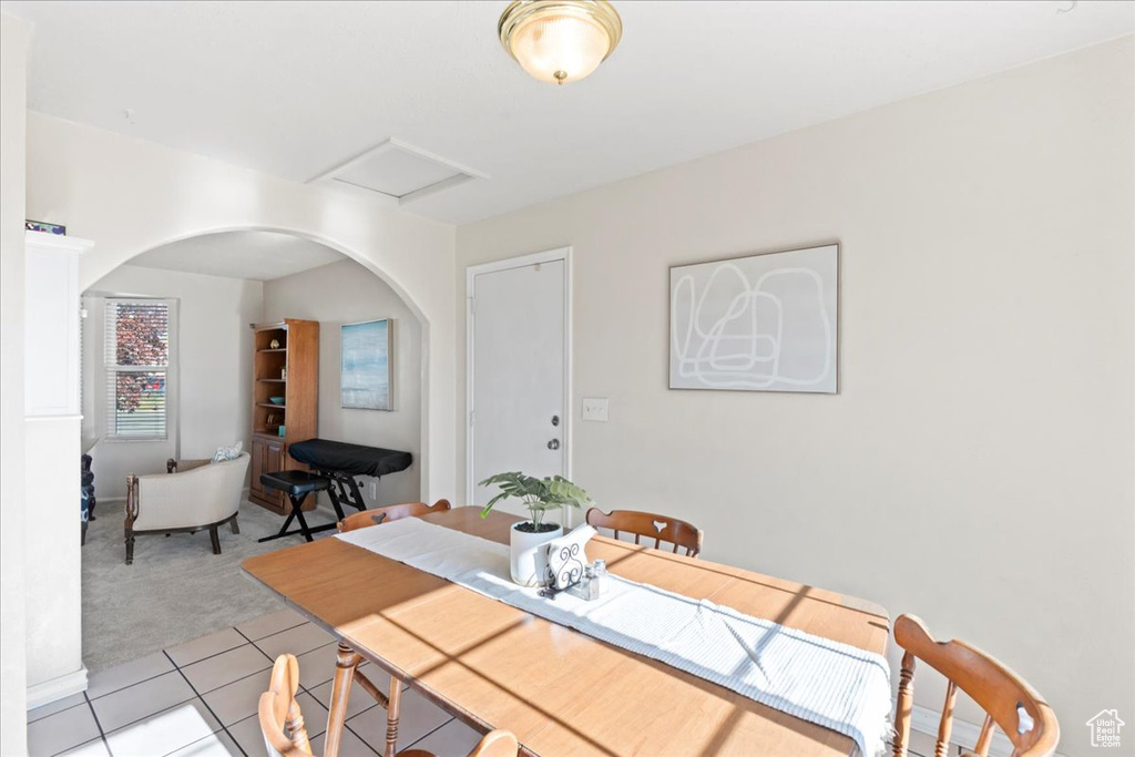 Dining area with light tile patterned floors, light colored carpet, attic access, and arched walkways