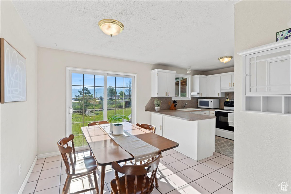 Kitchen featuring electric stove, white microwave, a sink, light tile patterned floors, and white cabinetry