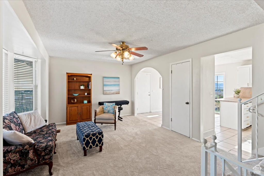 Living area featuring arched walkways, light carpet, a ceiling fan, and a textured ceiling