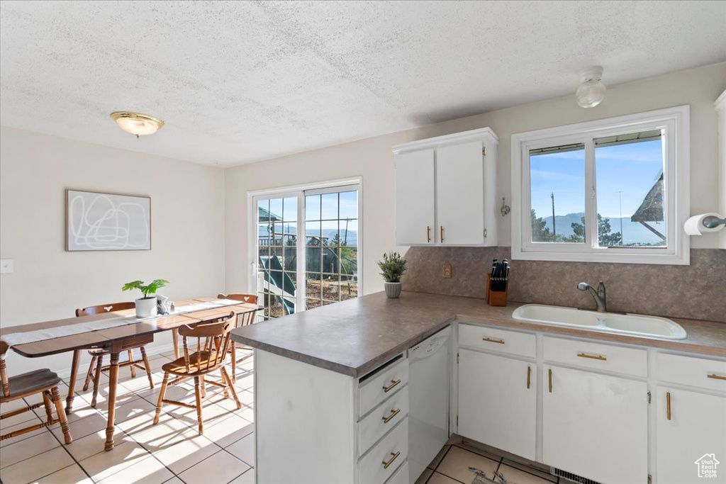 Kitchen featuring white dishwasher, a sink, a peninsula, a textured ceiling, and white cabinetry