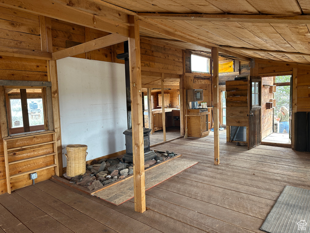 Misc room with lofted ceiling, a wood stove, hardwood / wood-style floors, healthy amount of natural light, and wooden walls