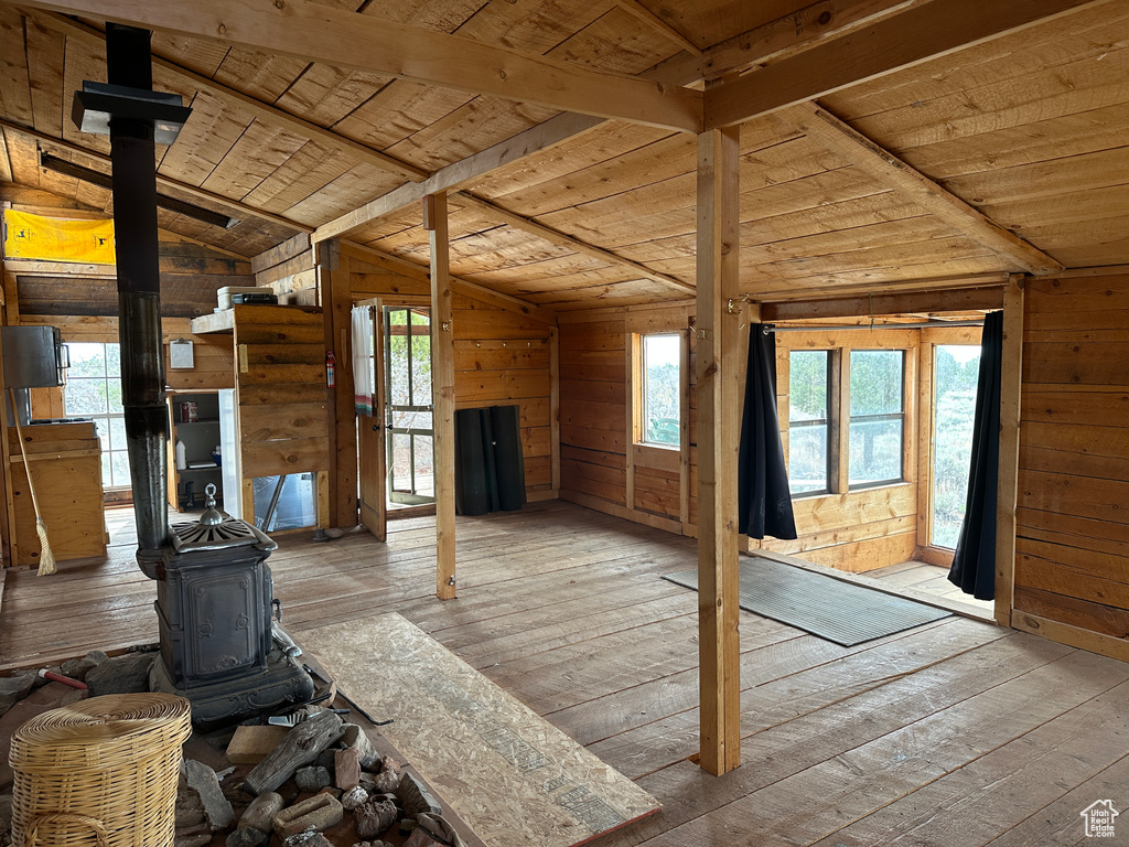 Unfurnished living room with a wood stove, wooden ceiling, hardwood / wood-style floors, and wood walls